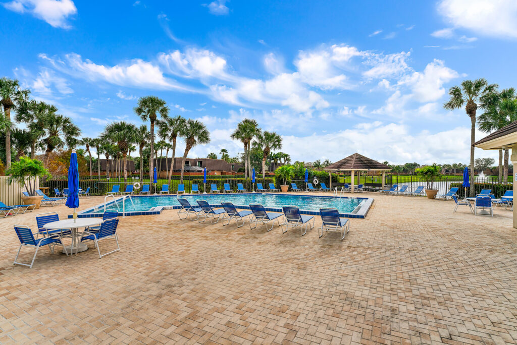 a pool surrounded by lounge chairs and palm trees at the back
